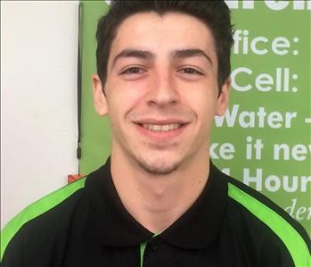 A young man with dark brown hair smiling in front of a SERVPRO of Claremont/Montclair banner.