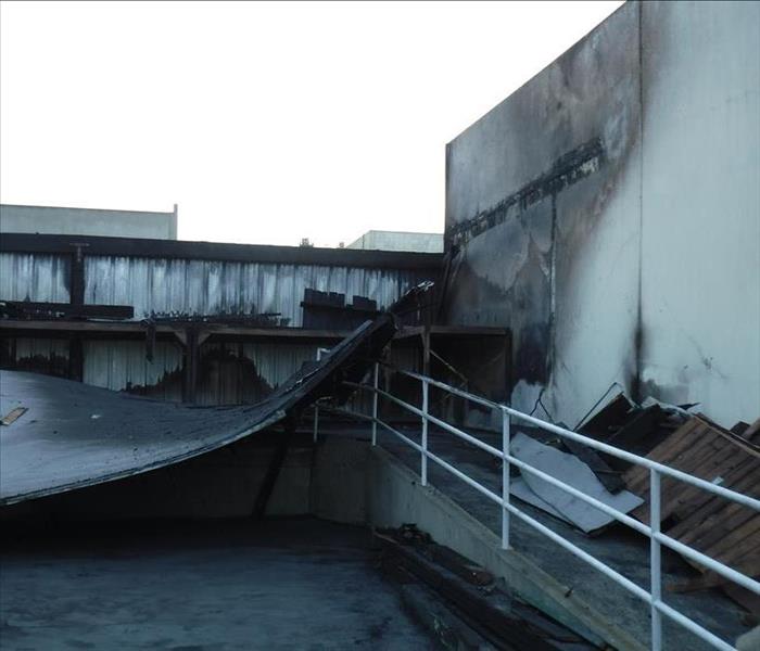 The outside of a burned commercial warehouse with a collapsing roof. 