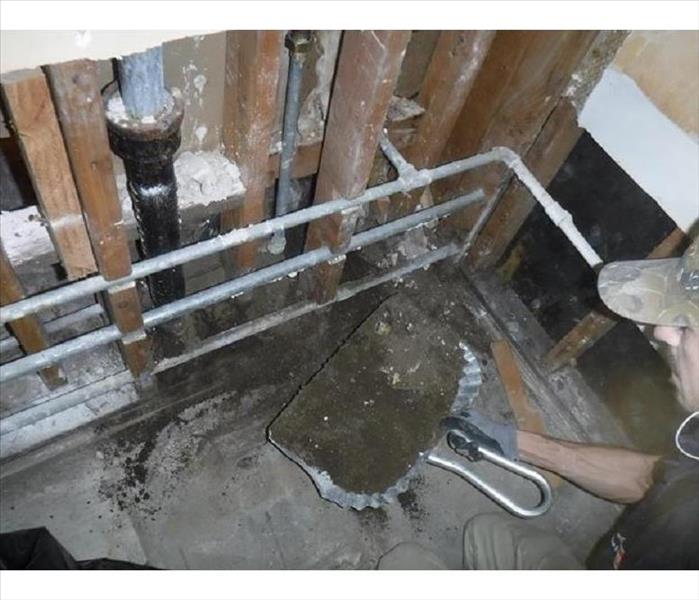 Frozen mud being dug out of an open wall with a silver dust pan by a technician.