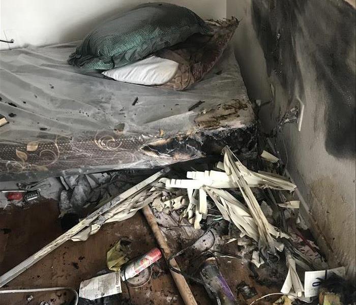 A corner of a room showing a burned twin mattress, two pillows and window blinds.