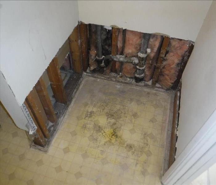 An open space where a water heater once was, with leftover insulation, a crooked cut on the drywall and half twisted metal.