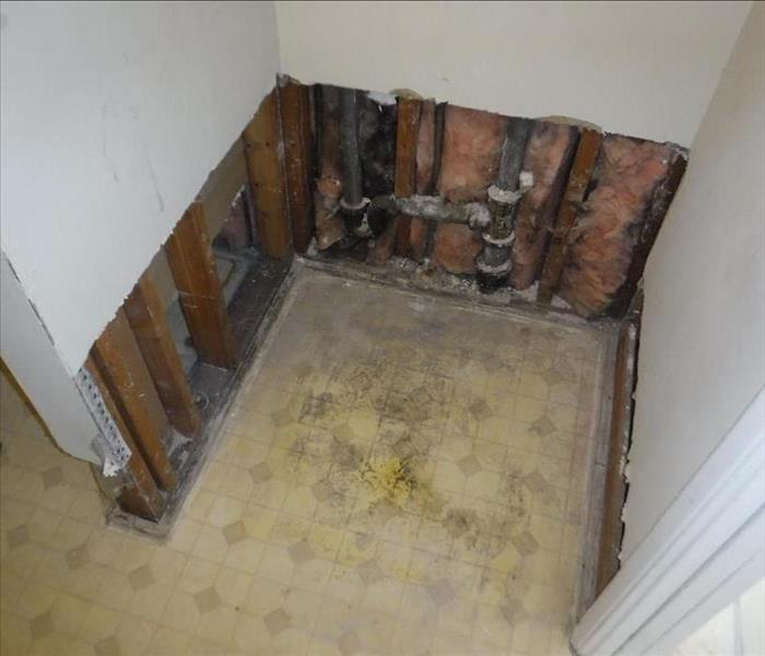 An open space where a water heater once was, with leftover insulation, a crooked cut on the drywall and half twisted metal.