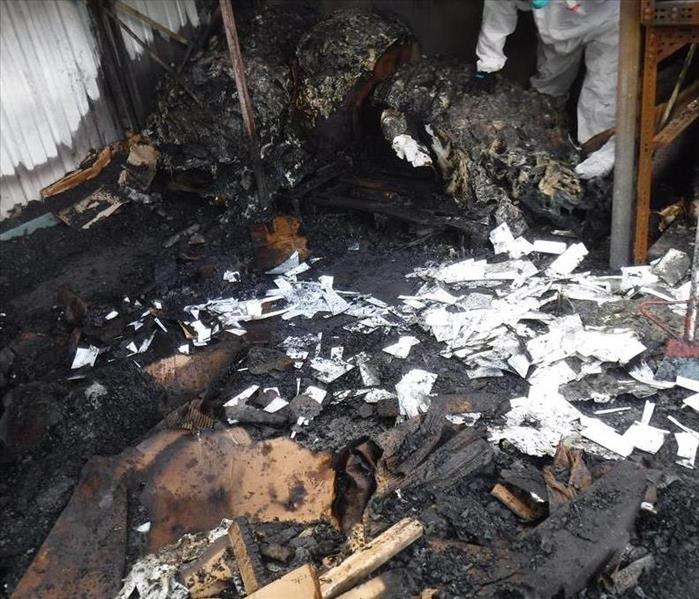 Burned wood, paper and debris. A technician in the far right corner picks up some of the burned debris.