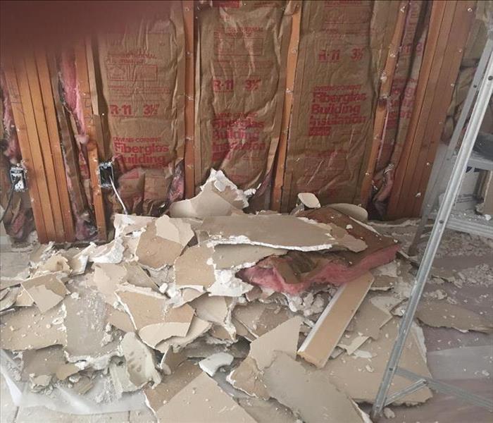 White drywall being demolished with new insulation and wood studs visible.