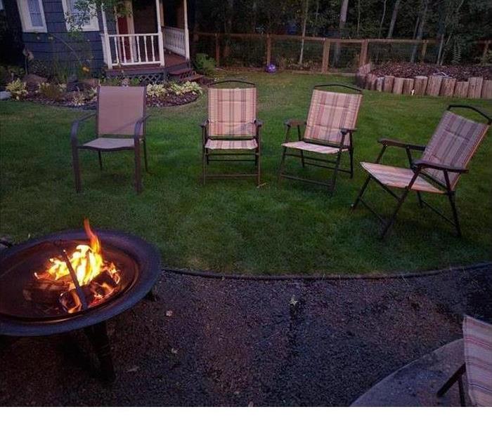 A fire pit burning with four chairs around it in a backyard. 
