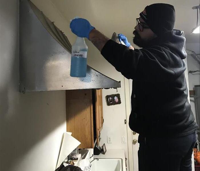 A technician with glasses wiping a stainless steel stove grease trap.