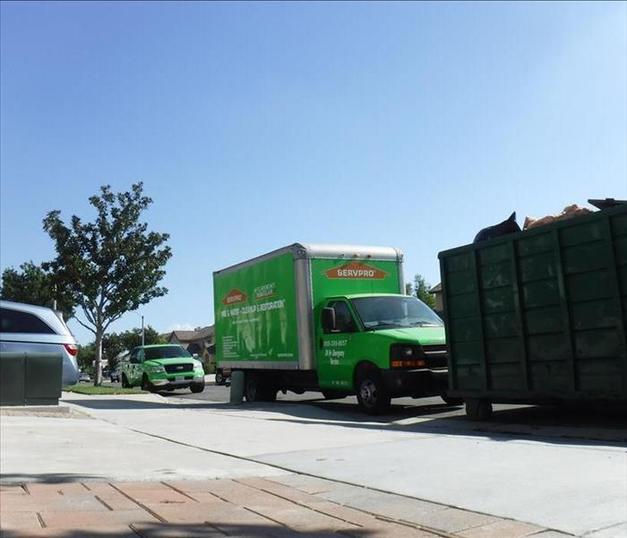 A green SERVPRO boxtruck and pickup truck parked in front of a wastebin.